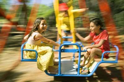 Tre bambini sorridenti su una giostra girevole in un parco giochi.