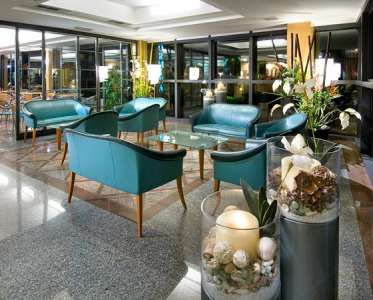 Salotto elegante con poltrone blu e tavoli, decorato con piante e candele.