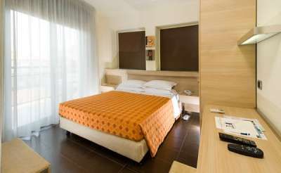 Camera d'albergo con letto matrimoniale e coperta arancione, arredamento moderno.