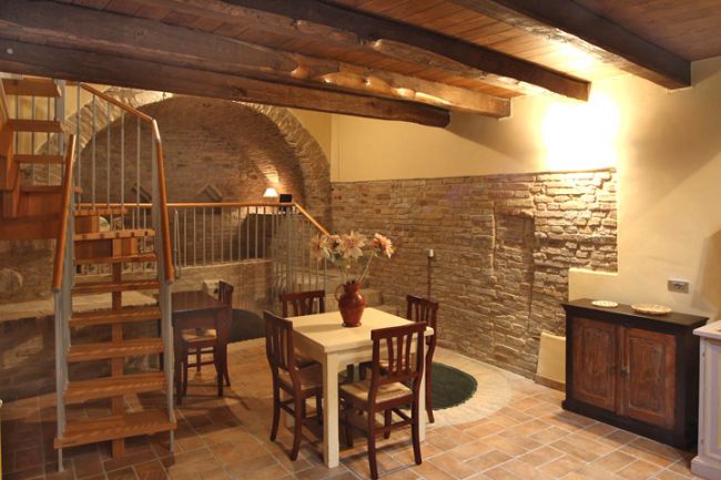Soggiorno con tavolo, scala e muri in pietra.