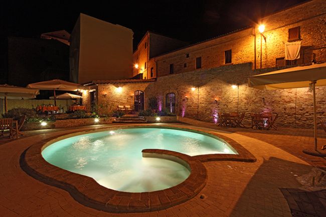 Piscina illuminata di notte con mura di mattoni.