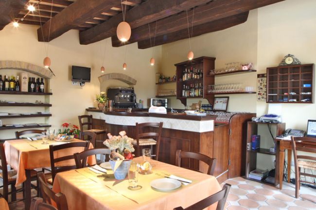 Sala ristorante accogliente con tavoli apparecchiati e bar.