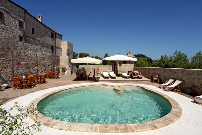 Piscina circolare con lettini e ombrelloni.