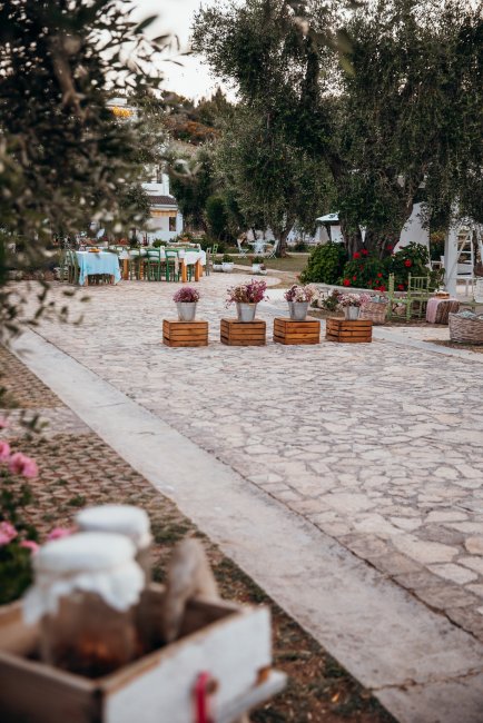 Pietraia con tavoli decorati e vasi di fiori, alberi e sedie sullo sfondo.