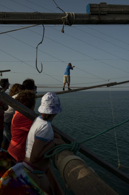 Persone osservano un uomo camminare su travi sopra il mare.