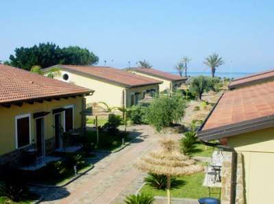 Villette con tetti rossi e giardini, vista sul mare in lontananza.