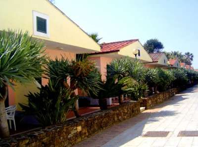 Villette gialle con tetti rossi e piante verdi lungo il marciapiede.