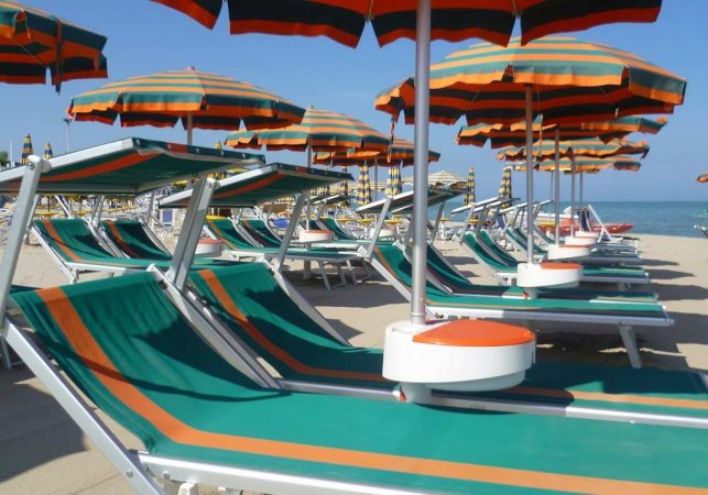 Lettini verdi sotto ombrelloni color arancio e verde su una spiaggia soleggiata.