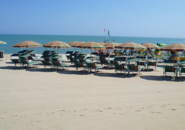 Spiaggia con lettini e ombrelloni arancioni e verdi di fronte al mare calmo.