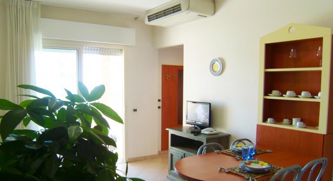 Interno di un appartamento con tavolo apparecchiato, pianta e piccolo televisore.