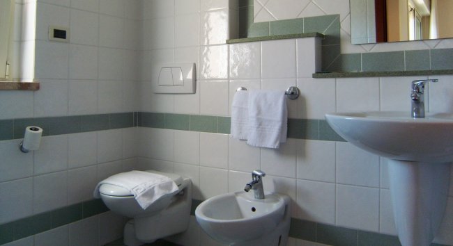 Bagno semplice con wc, bidet, lavandino e asciugamano bianco su un portasciugamani.