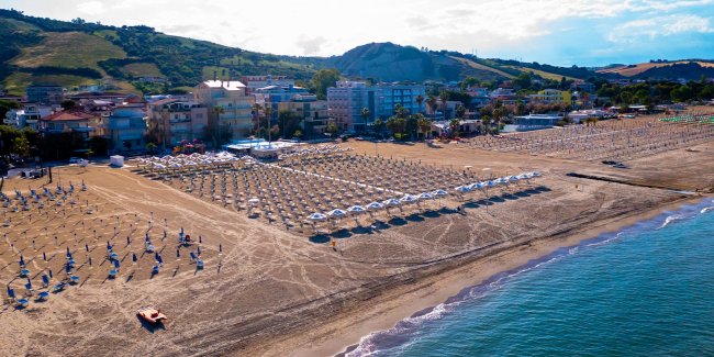 Spiaggia con ombrelloni e vista su colline e edifici.