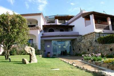 Una villa su due livelli con balconi, giardino curato e pietre decorative.
