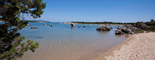 Spiaggia sabbiosa con mare calmo e rocce.