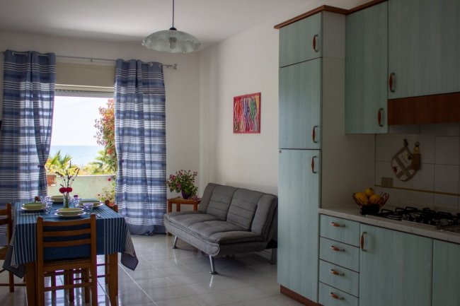 Cucina-soggiorno con tavolo, divano e vista sul mare.