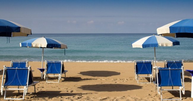 Spiaggia con sedie a sdraio e ombrelloni blu.