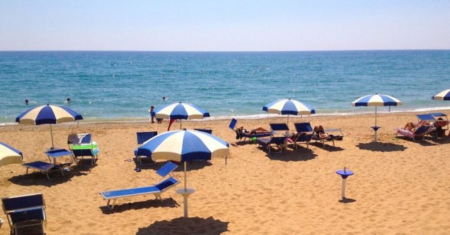 Spiaggia affollata con sdraio e ombrelloni blu.