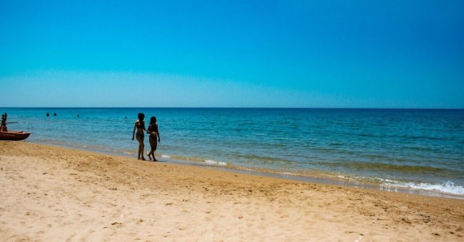 Due persone camminano su una spiaggia sabbiosa.