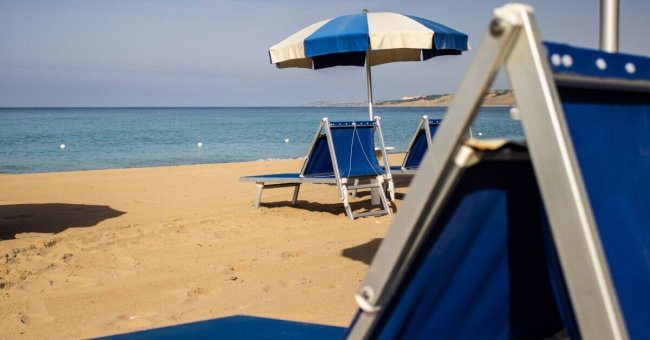 Spiaggia con lettini blu e ombrellone a righe.