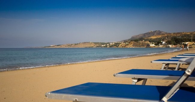 Spiaggia deserta con lettini blu e mare calmo.