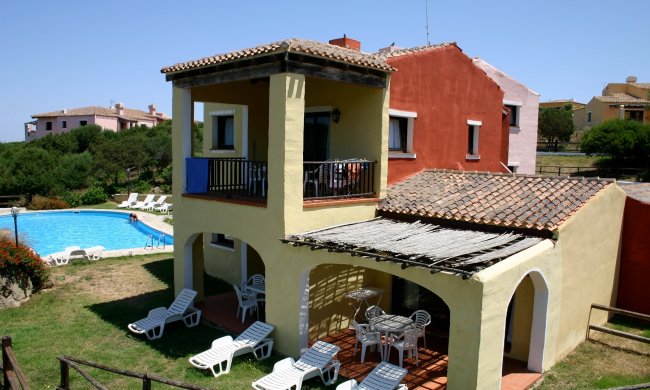 Casa con portico e piscina, lettini bianchi.