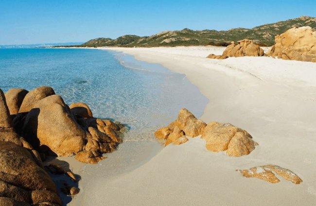 Spiaggia di sabbia bianca e rocce marroni.