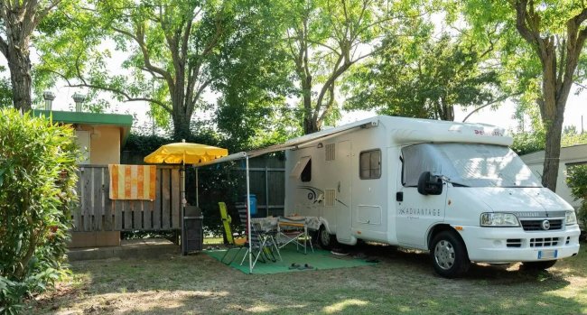 Camper parcheggiato all'aperto con ombrellone e sedie.