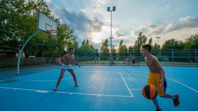 Due ragazzi giocano a basket su un campo esterno.