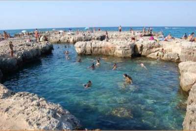 Persone nuotano in una piscina naturale rocciosa vicino al mare.