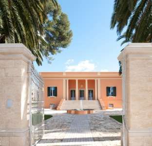 Villa arancione con colonne bianche, circondata da palme e un vialetto di pietra.
