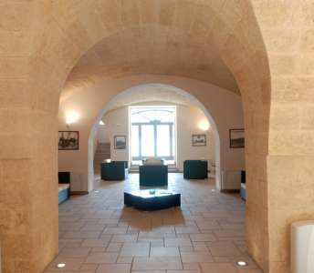 Interno di una sala con ampio arco, pavimento in pietra e arredamento sobrio.