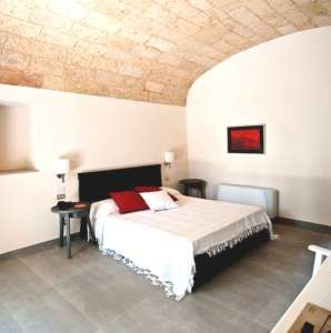 Camera da letto con soffitto in pietra, letto matrimoniale e pareti bianche.