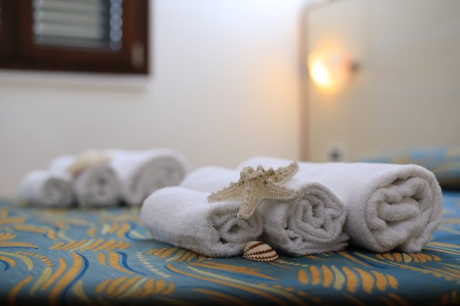 Asciugamani bianchi arrotolati su un letto, decorati con una stella marina.