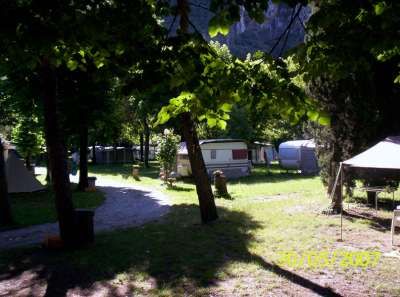 Area campeggio con roulotte, tenda e alberi verdi.