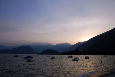 Lago al tramonto con barche ormeggiate e montagne sullo sfondo.