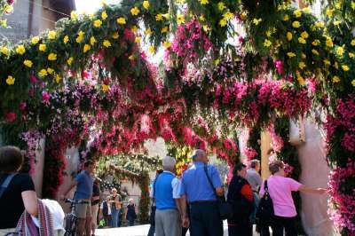 Un arco decorato con fiori rosa e gialli, sotto cui passano persone.