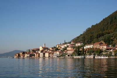 Un villaggio pittoresco con case color pastello lungo il lago, circondato da colline verdi.