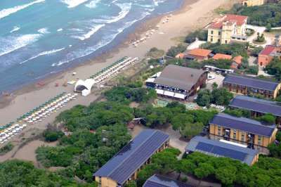 Vista aerea di una spiaggia sabbiosa con file di ombrelloni e edifici circondati da vegetazione.