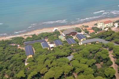Complesso di edifici tra alberi, vicino a una lunga spiaggia sabbiosa con ombrelloni.