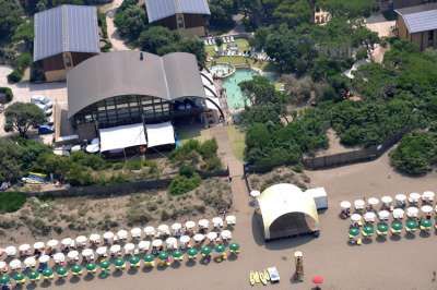 Vista aerea di una struttura sulla spiaggia con piscine e ombrelloni allineati sulla sabbia.