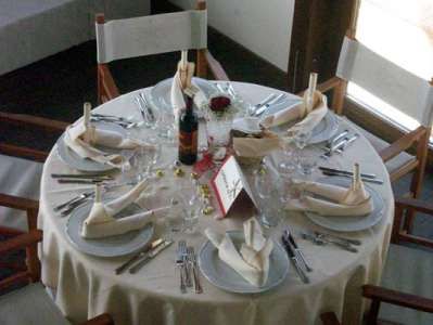 Tavola rotonda apparecchiata con piatti, posate, bicchieri, tovaglioli e una bottiglia di vino.