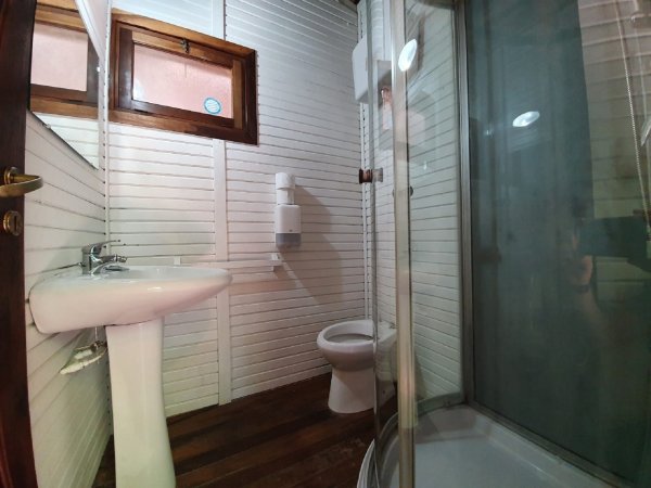 Bagno con doccia, lavandino e WC, pareti in legno bianco.
