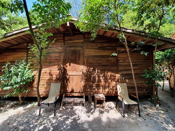 Casetta di legno con due sedie all'esterno, circondata da alberi.