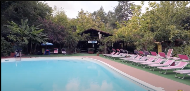 Piscina all'aperto con lettini rosa e vegetazione rigogliosa intorno.