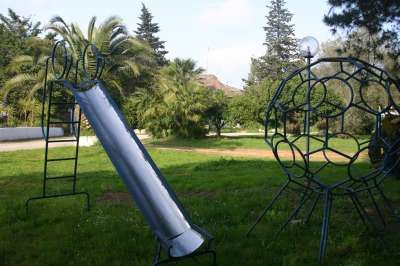 Un parco giochi con scivolo e struttura metallica, circondato da palme e alberi.