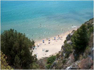 Spiaggia vista dall'alto con ombrelloni e mare azzurro.