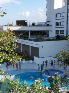 Piscina affollata accanto a un edificio moderno e piante.