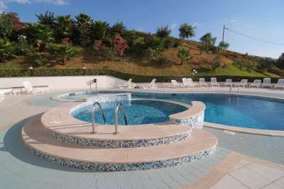 Piscina vuota con area idromassaggio, circondata da sedie a sdraio.