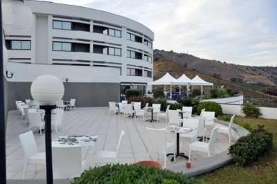 Terrazza di un edificio bianco con tavoli e sedie, colline sullo sfondo.