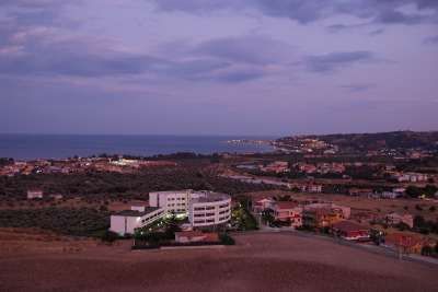 Panorama costiero con mare, edifici e colline al tramonto.